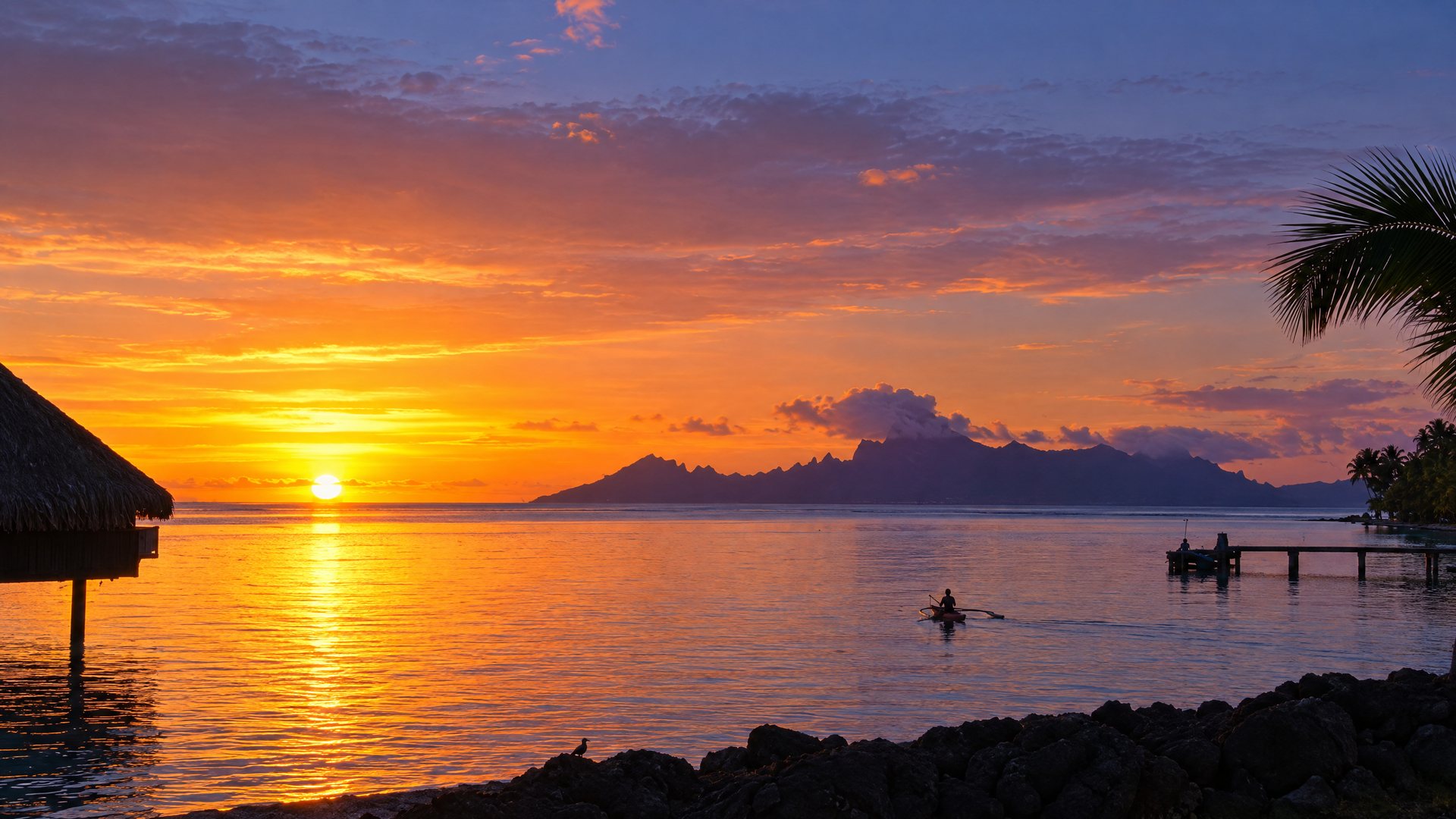 Sunset over Moorea seen from Tahiti's west coast, a lone outrigger canoe on the water